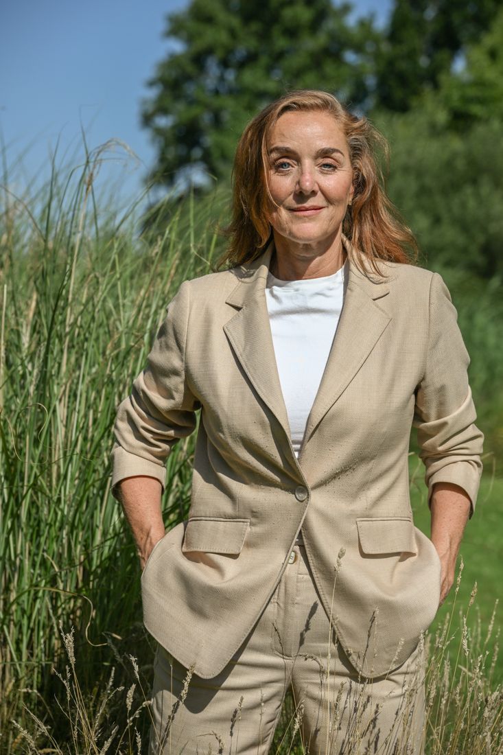 Judith Appelman in een beige pak, buiten tussen hoog gras